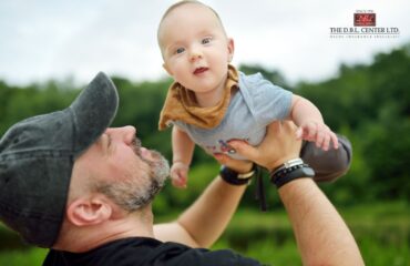 GenX dad or granddad holding up a baby son in the air.