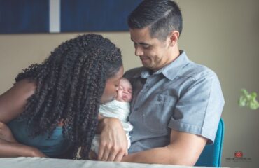 A father is holding an infant while the mother kisses the baby's cheek - family bonding at its best.