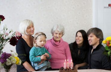 Sandwich generation caregiving Four generations at a table, celebrating a mother's 100th birthday.