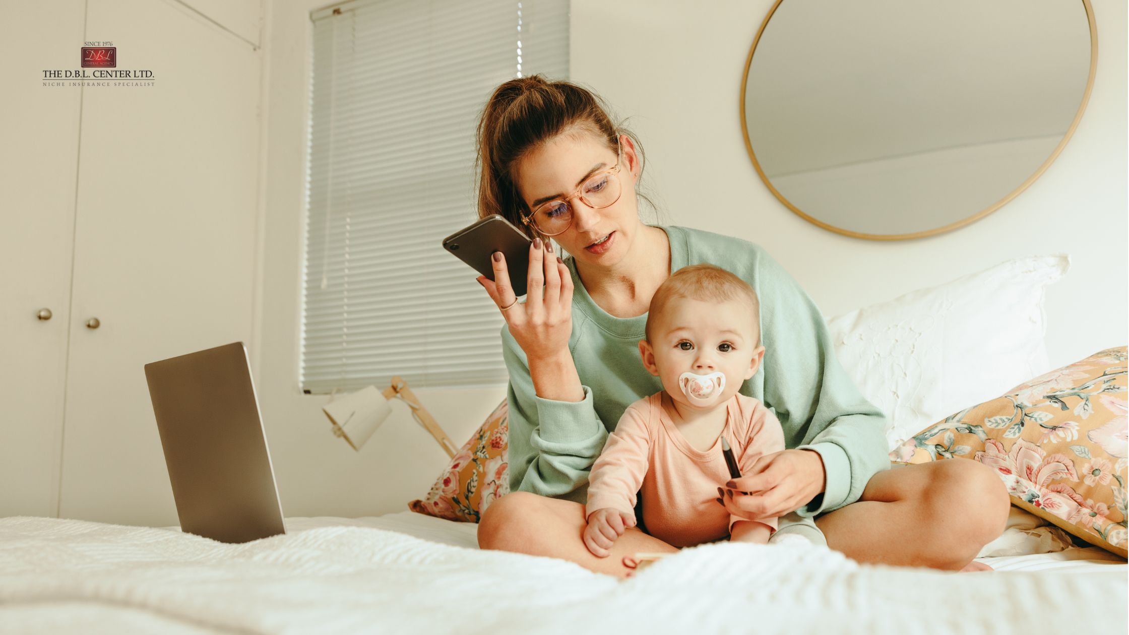 Paid Leave in NY Tik Tok Myths Mom with an infant on her lap, sitting on a bed, laptop open next to her. The mom is on her phone.